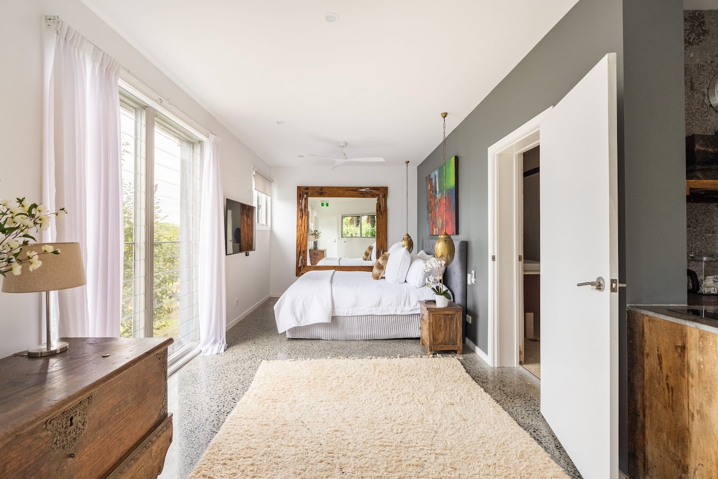 A bright Villa bedroom with timber furnishings and windows opening towards the estate grounds.