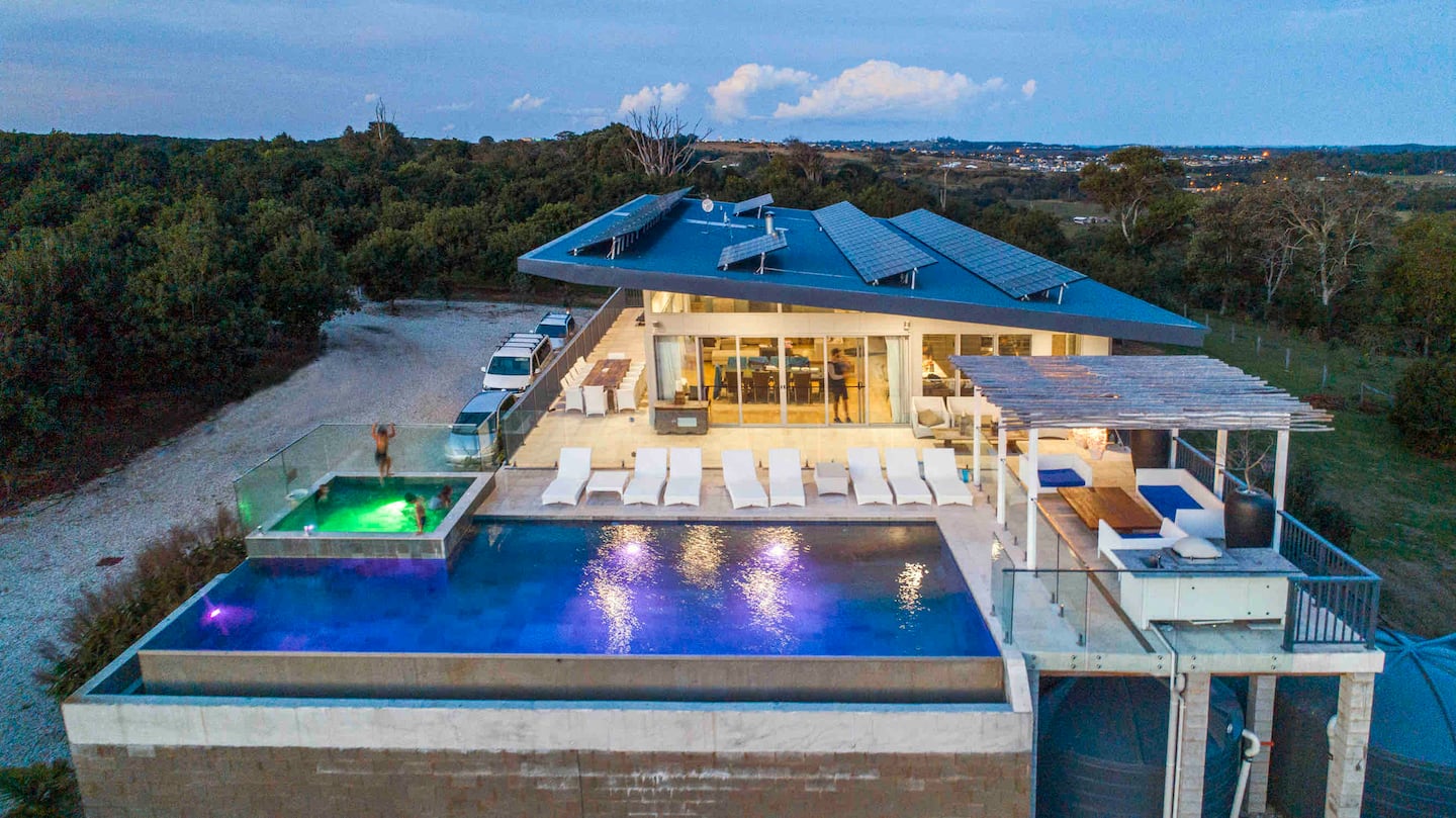 The illuminated Tides Villa, infinity pool and terrace at dusk, with the orchard and hills behind.